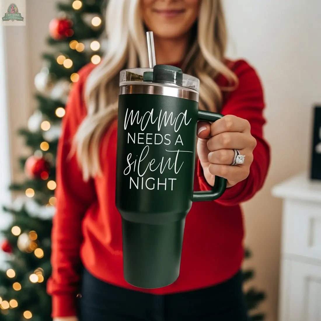 A woman in a red sweater holds the Silent Night 40oz dark green insulated mug with a straw and "Mama needs a silent night" in white script. A blurred, decorated Christmas tree in the background makes this an ideal Christmas gift.
