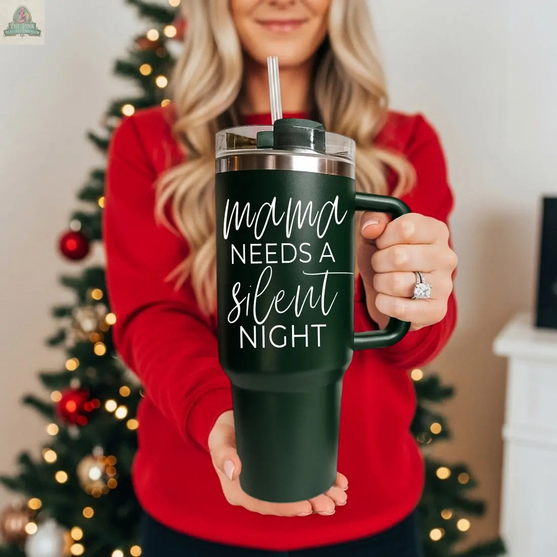 A woman in a red sweater stands by a decorated Christmas tree, holding a green Silent Night 40oz tumbler—perfect as a cozy holiday gift with "Mama needs a silent night" written on it.