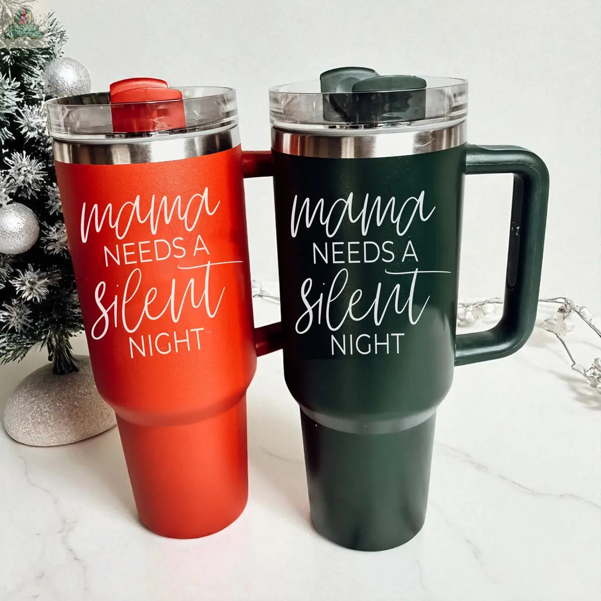 Two Silent Night 40oz insulated mugs, one red and one dark green with “mama needs a silent night” in white script, stand side by side amid festive décor and a small Christmas tree—perfect for Christmas gifting.