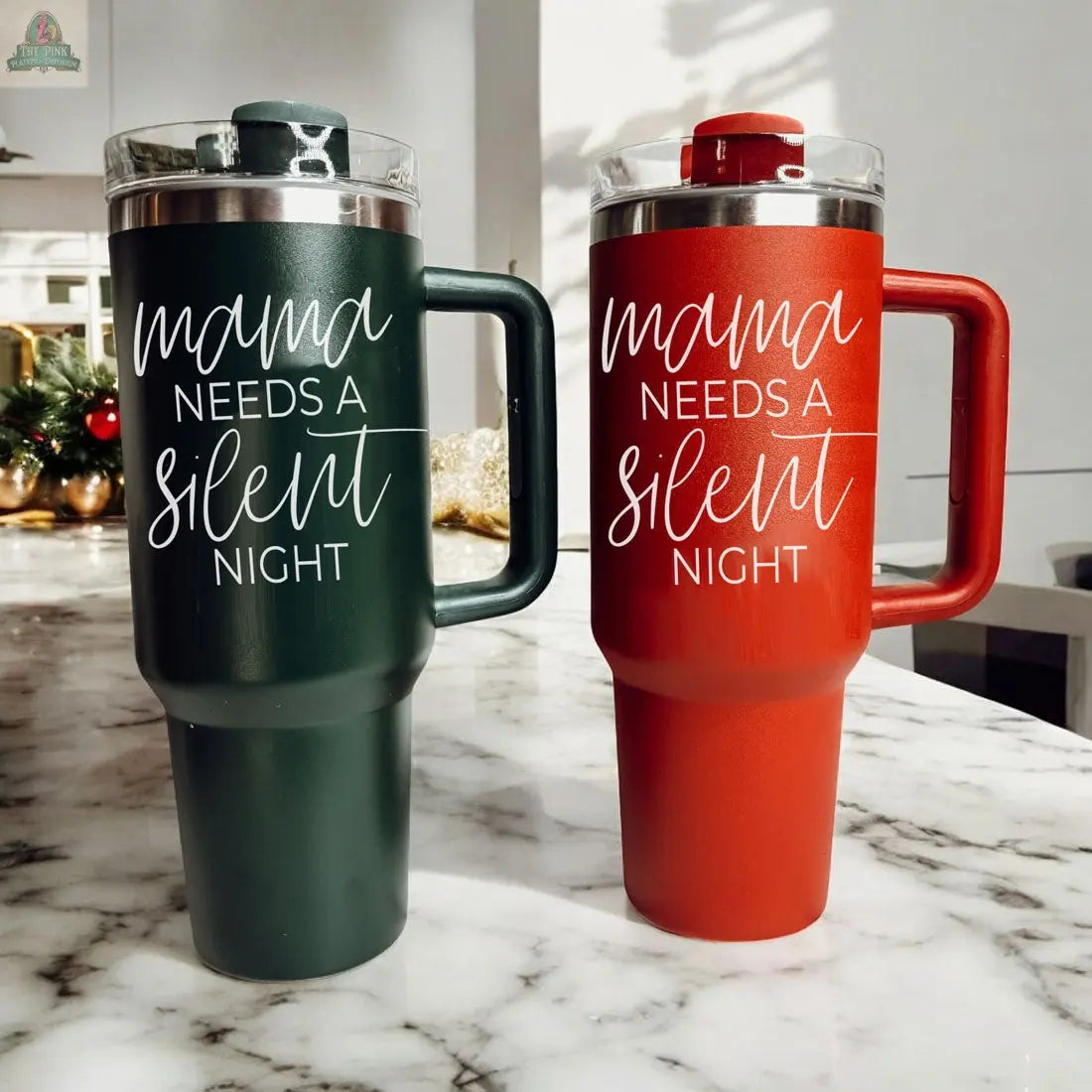 Two Silent Night 40oz insulated mugs—one dark green and one red, both featuring "Mama needs a silent night" in white script—sit on a marble countertop, making them the perfect cozy Christmas gift.