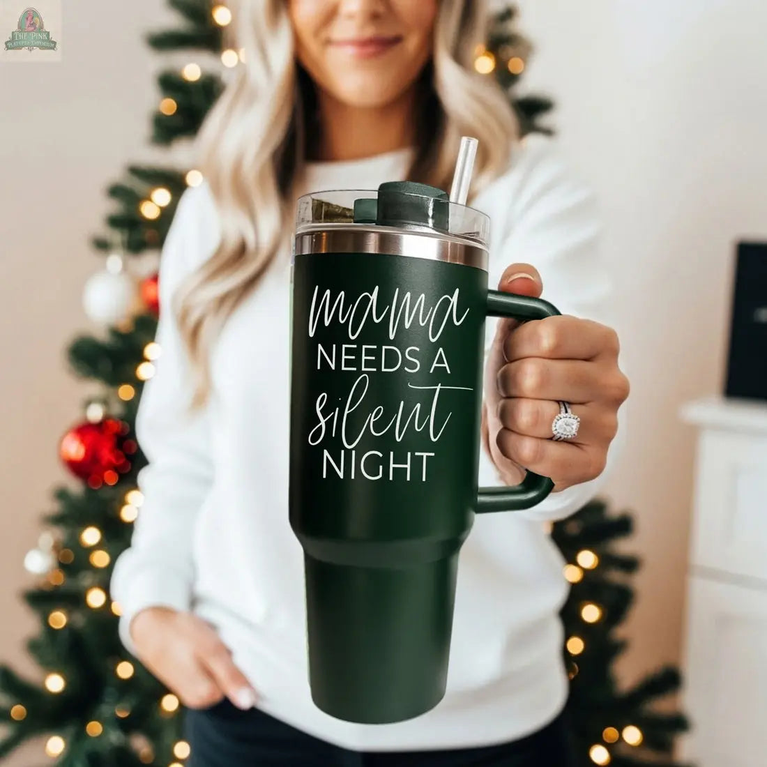 A woman in a white sweater stands before a decorated Christmas tree, holding a Silent Night 40oz insulated mug featuring the words "Mama needs a silent night"—a perfect Christmas gift.