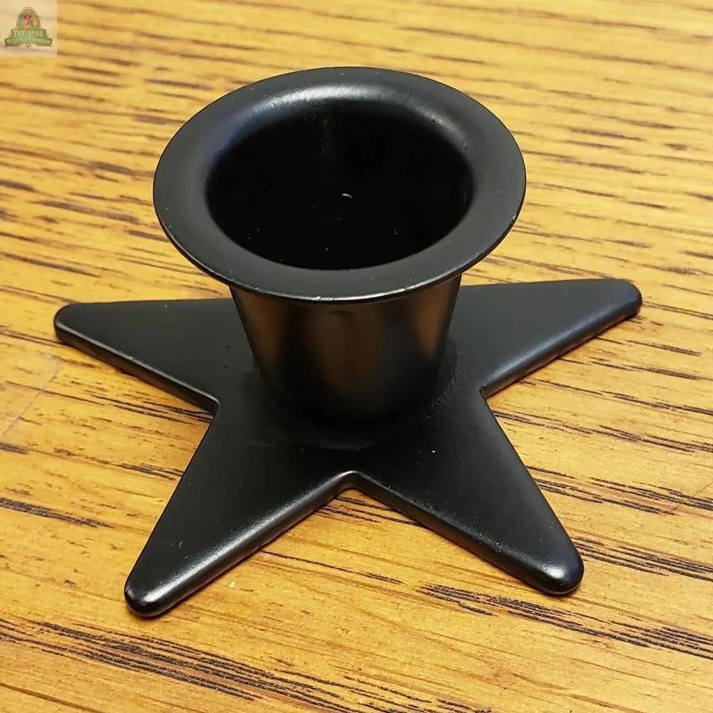 The Small Metal Star Taper Holder, made of black metal with a round opening, rests on a wood surface featuring visible grain patterns.