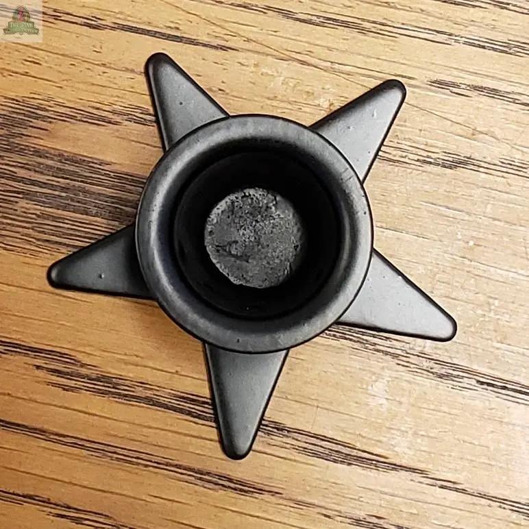 The Small Metal Star Taper Holder, crafted from black metal with a round center, rests on a dark-grained wooden surface.