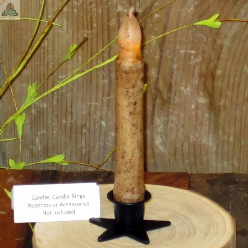 A Small Metal Star Taper Holder with a rustic brown candle stands on wood, framed by green leafy branches. A sign notes: "Candle, Candle Rings, Rosehips or Accessories Not Included.