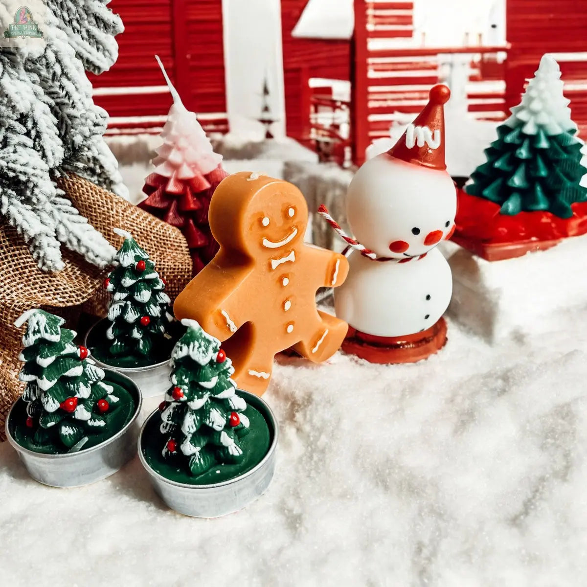 A festive scene featuring a gingerbread man, the Snowman Candle, and Christmas tree candles on artificial snow, with a red and white house and snowy branches—perfect winter home decor.
