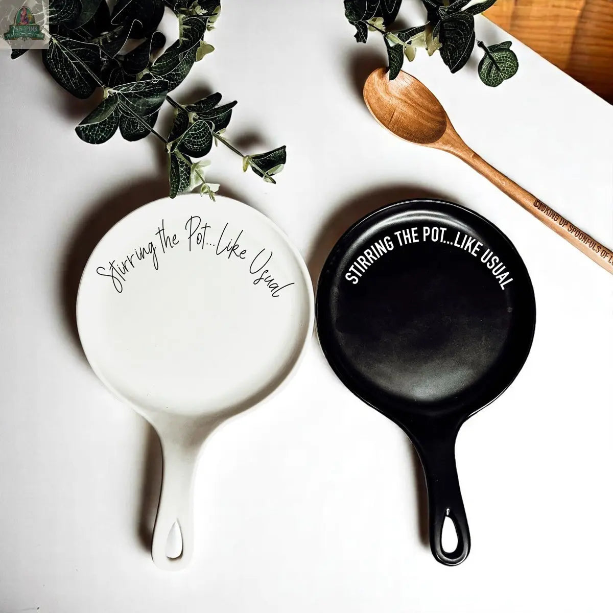 The “Stirring the Pot” set features two frying pans, one white and one black, side by side with “Stirring the pot...like usual” on them—a funny, quirky porcelain kitchen gift for any home chef. A wooden spoon completes this unique accessory.