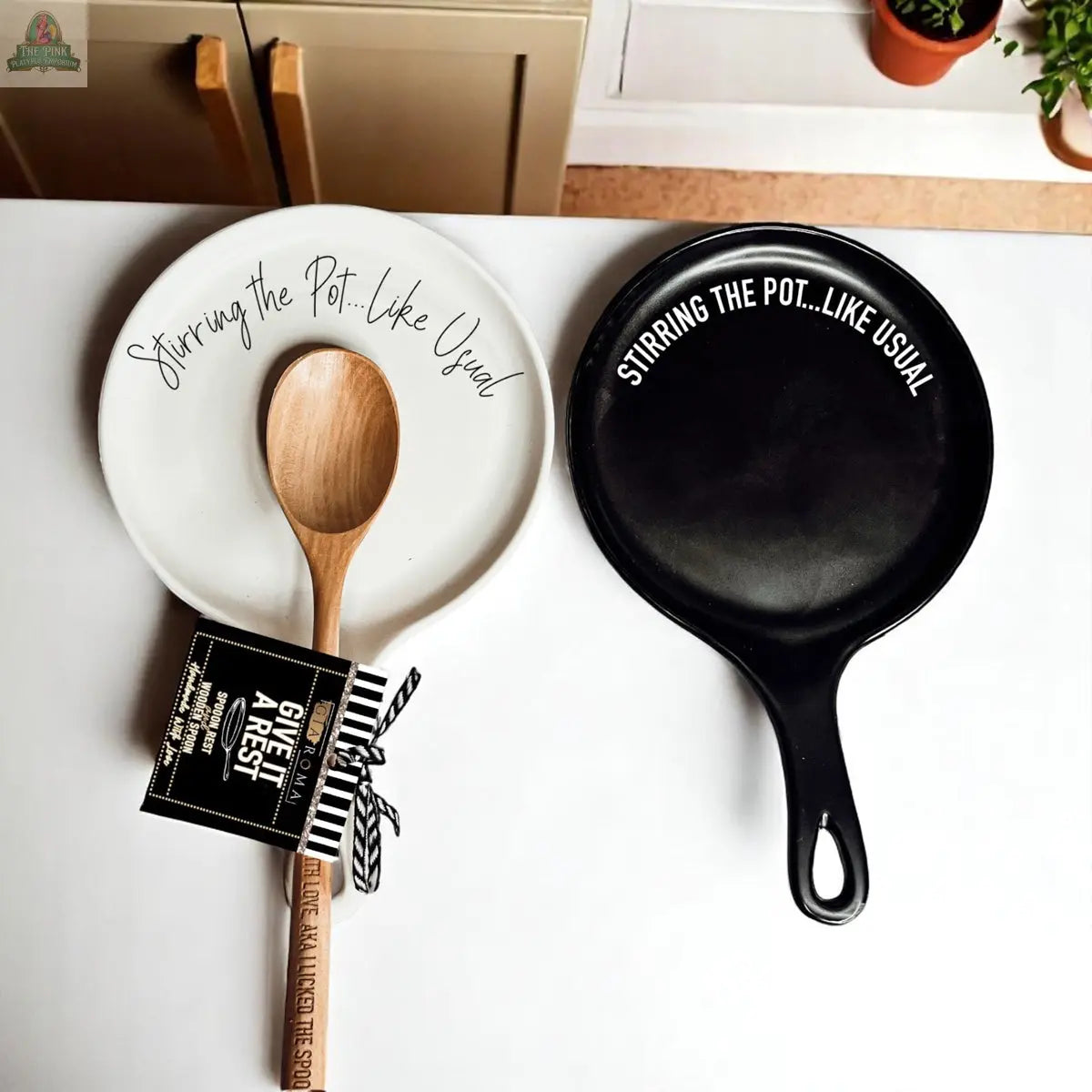 The Stirring the Pot set features a white plate with cursive text, a wooden spoon, and a black skillet—all arranged for a charming kitchen gift or a unique porcelain spoon rest.