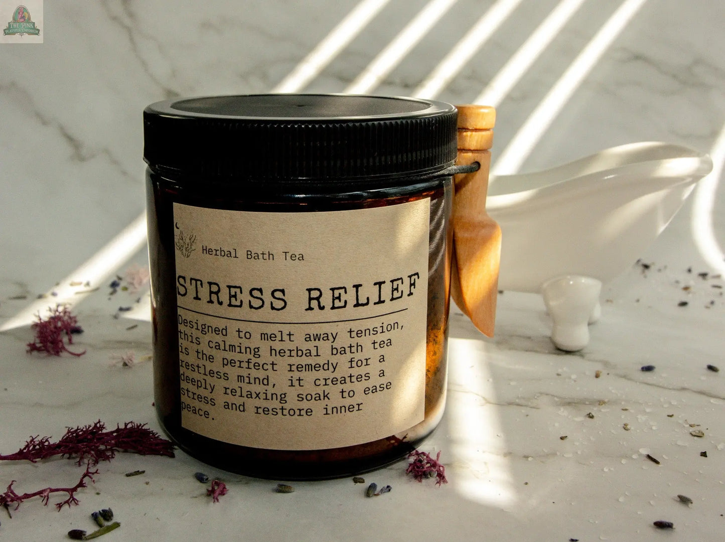 A jar of Stress Relief bath tea rests on marble with dried flowers and a wooden scoop, ideal for an Epsom salt soak. Soft sunlight and gentle shadows create a calming, serene scene.