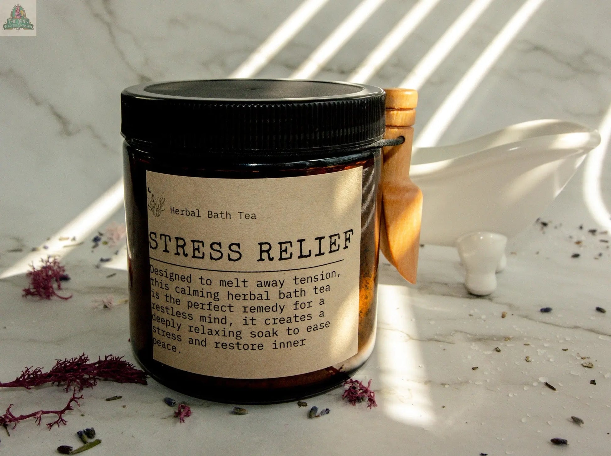 A jar of Stress Relief bath tea rests on marble with dried flowers and a wooden scoop, ideal for an Epsom salt soak. Soft sunlight and gentle shadows create a calming, serene scene.