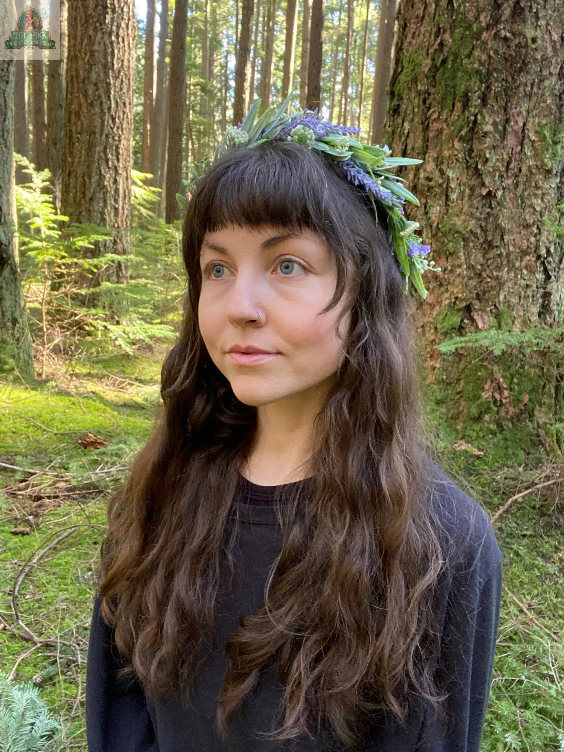 A woman with long brown hair, in a leafy flower crown and black shirt, stands in a sunlit forest—evoking nature’s quiet magic—featured on the REDFeather Animystic Tarot Deck Box Set.