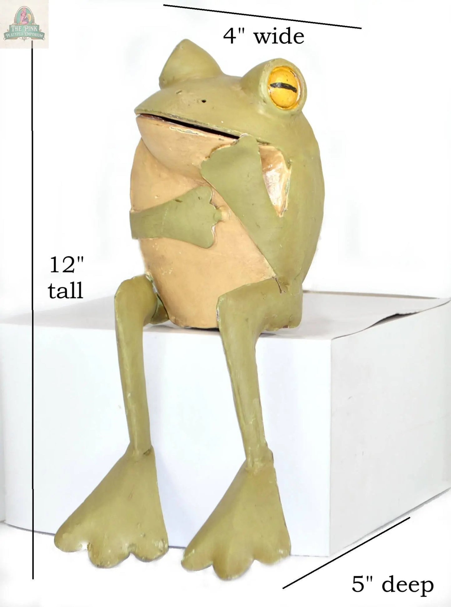 The Thinking Frog figurine is an 11" hand-painted metal décor piece featuring long legs, large yellow eyes, and a relaxed pose. It sits atop a white box labeled 5" deep, making it a unique accent for any space.