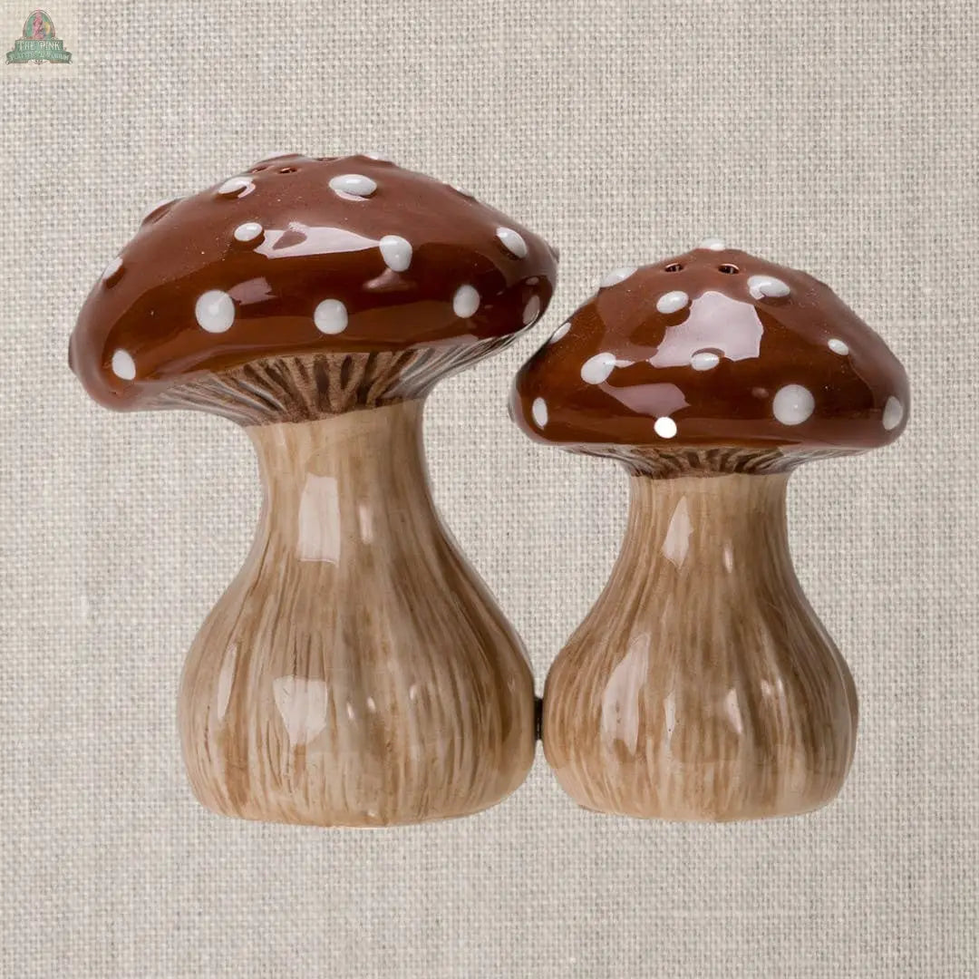 The Toadstool Mushrooms Salt and Pepper Shaker Set features two brown shakers with white spots, shaped like mushrooms and displayed on a textured beige background—an adorable addition to any kitchen décor.