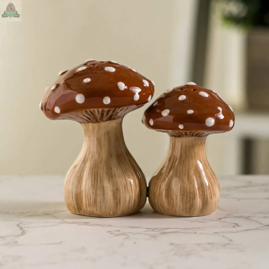 The Toadstool Mushrooms Salt and Pepper Shaker Set features charming brown ceramic mushrooms with white spots, adding a whimsical touch to your kitchen décor. Perfect for display on any countertop or dining table.