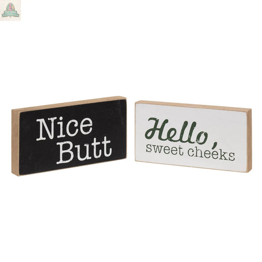 The Toilet Block Sign Assorted/2 set features two rustic wood blocks with fun quotes—one black with “Nice Butt” in white, and one white with “Hello, sweet cheeks” in green and black—perfect for humorous bathroom decor.