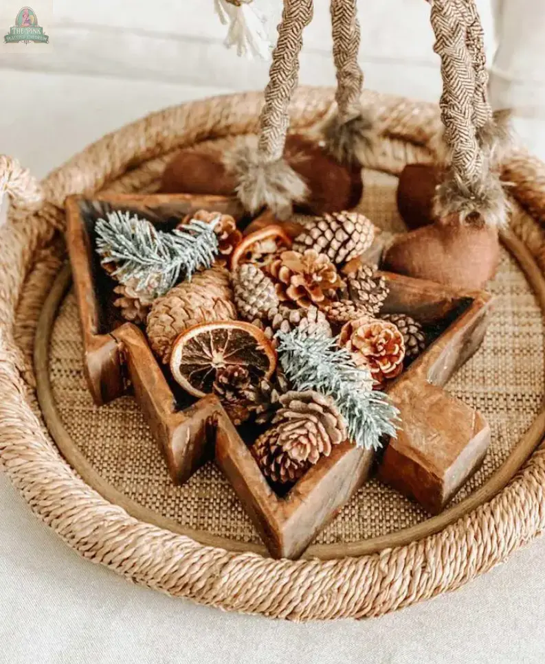 A woven tray displays the Tree Dough Bowl, Handmade, #A—a wooden, Christmas tree-shaped bowl filled with pinecones, dried orange slices, and frosted greenery. Decorative rope legs with tassels are visible in the background.