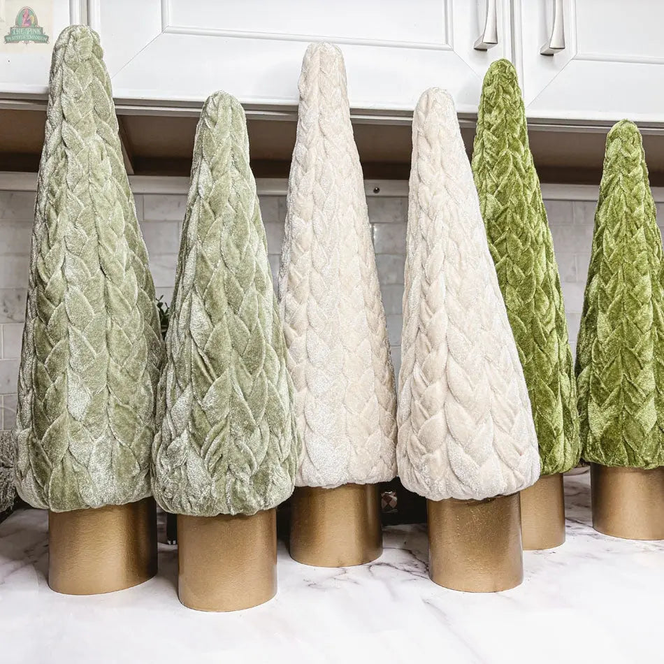 Velvet Christmas Trees in green and ivory, each with a gold cylindrical base, add charming holiday decor to a marble countertop under white kitchen cabinets—perfect for a farmhouse-style touch.