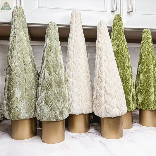 Velvet Christmas Trees in green and ivory, each with a gold cylindrical base, add charming holiday decor to a marble countertop under white kitchen cabinets—perfect for a farmhouse-style touch.