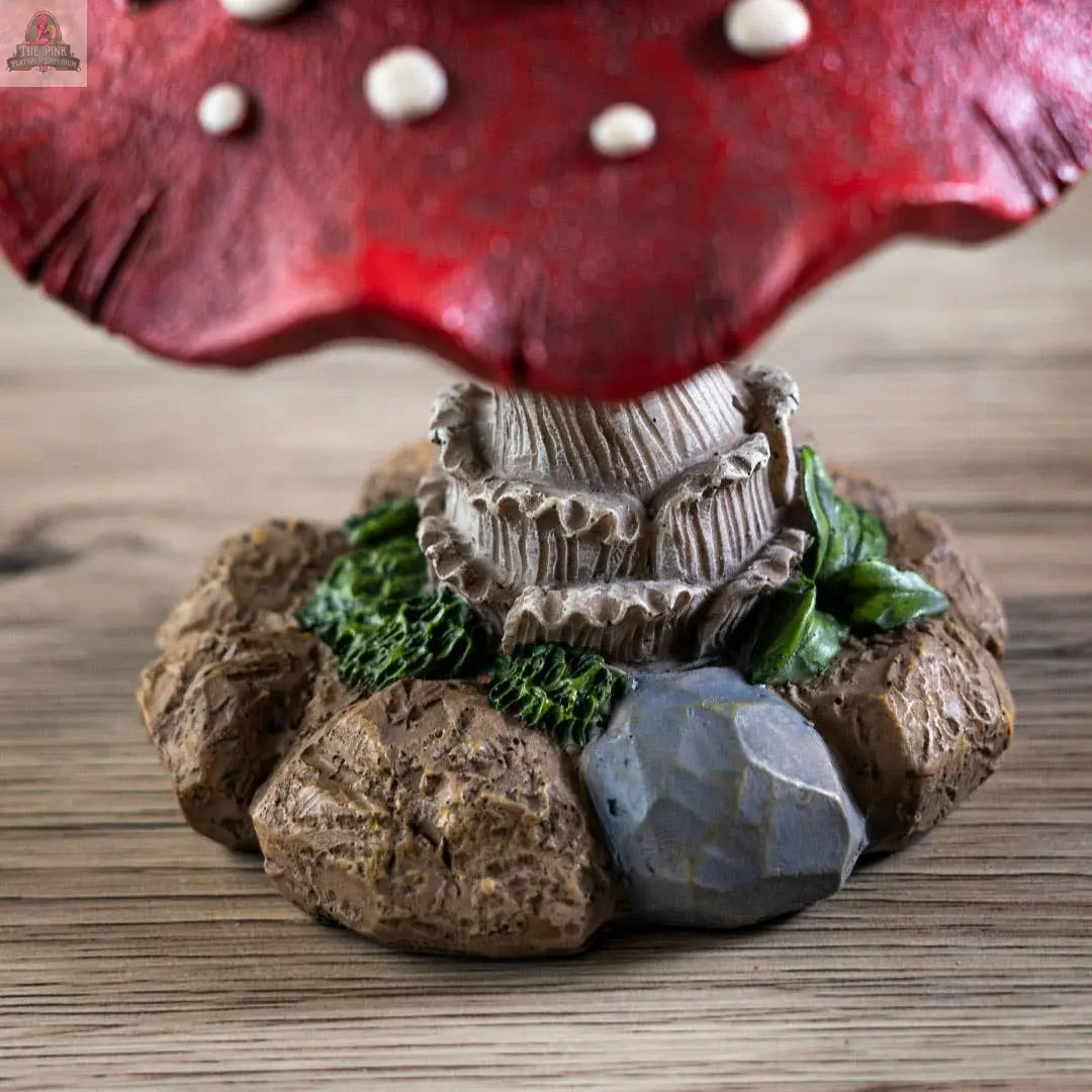 A close-up of the Whimsical Toadstool Mushroom Home and Garden Decor, featuring a red cap with white spots, detailed gills, a grayish stalk, and a textured rocky base with green moss—an enchanting cottagecore accent for your space.