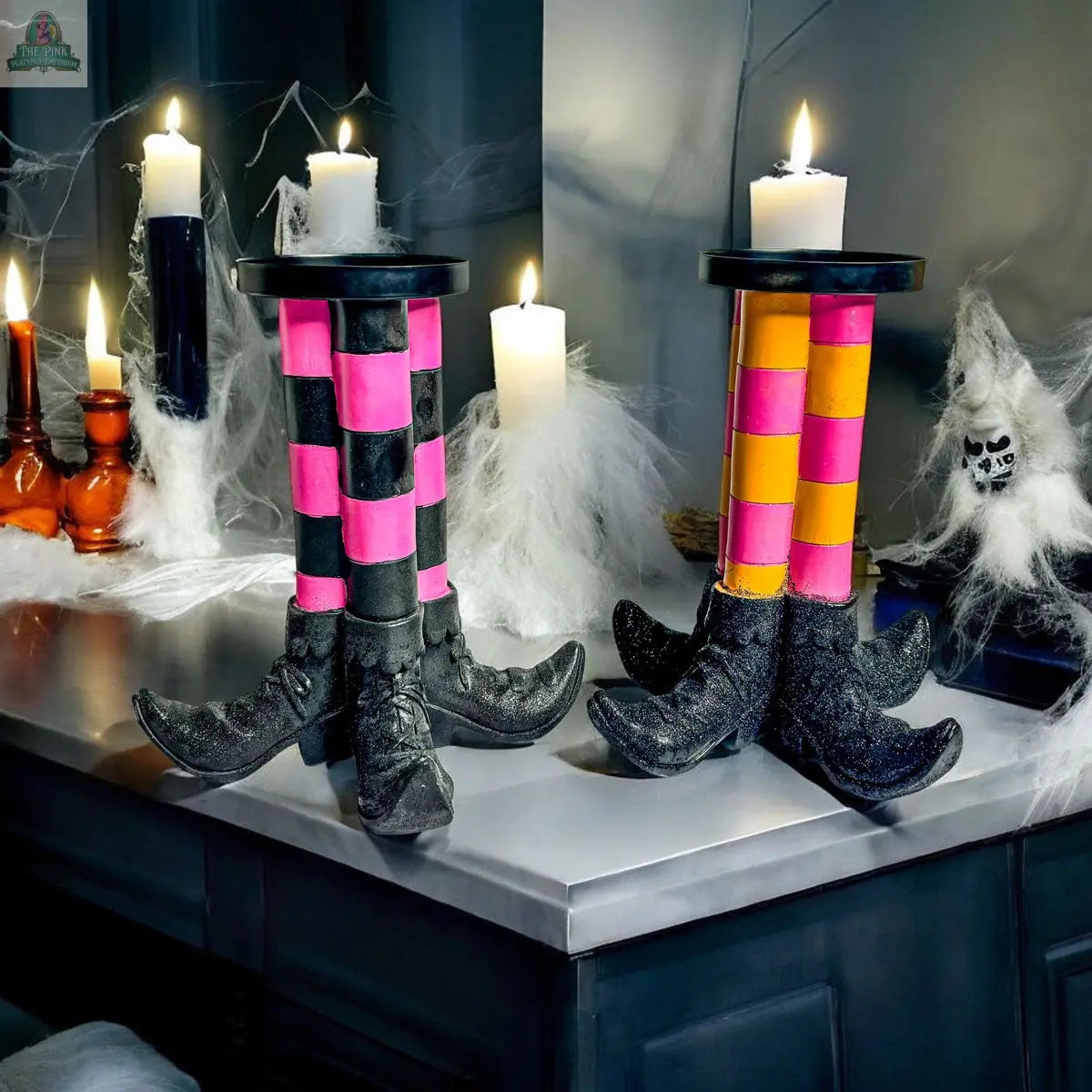 The Wicked Witch Candle Holder, featuring quirky witches’ legs with striped stockings, black pointed shoes, and pink-and-yellow checkered patterns, makes a whimsical Halloween centerpiece among candles and cobwebs.