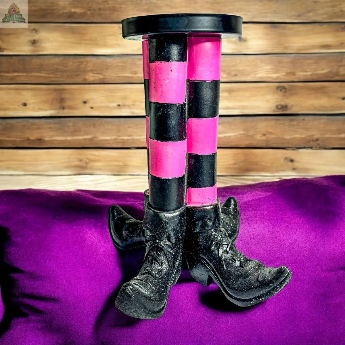 The Wicked Witch Candle Holder features black and pink striped legs with boots perched on a purple pillow, creating a quirky Halloween centerpiece for your spooky decor.