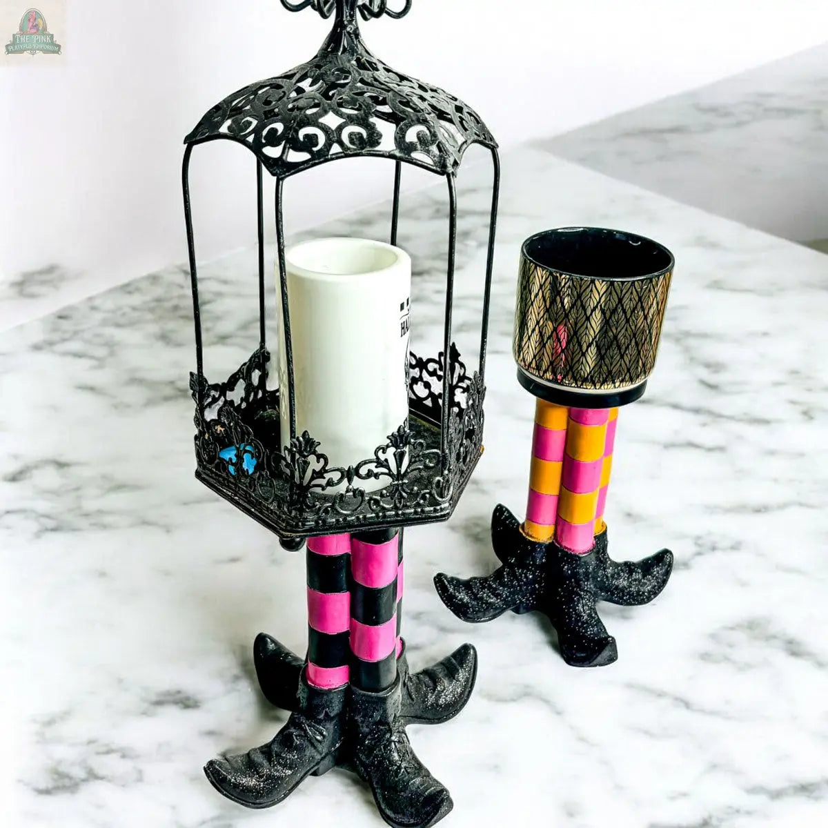 The Wicked Witch Candle Holder with ornate black legs and a white candle in a filigree metal cage creates a striking Halloween centerpiece on a marble surface.