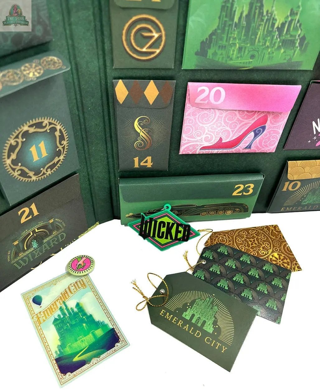 Wicked: The Official Advent Calendar features numbered green and gold pockets, a pink shoe illustration, Emerald City cards, tags, and a green Wicked ornament—perfect for Oz fans or Wicked collectors seeking unique gifts.
