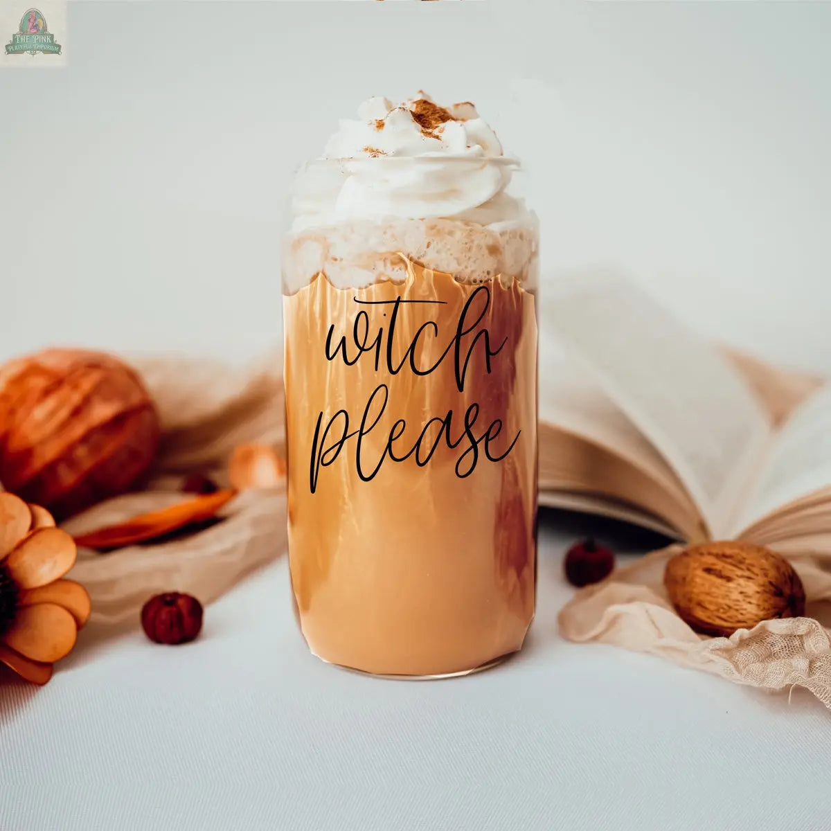 The Witch Please 17oz glass cup features a pumpkin latte with whipped cream, cinnamon, bamboo lid, and stainless steel straw, set among pumpkins, nuts, orange flowers, and an open book in cozy autumn decor.