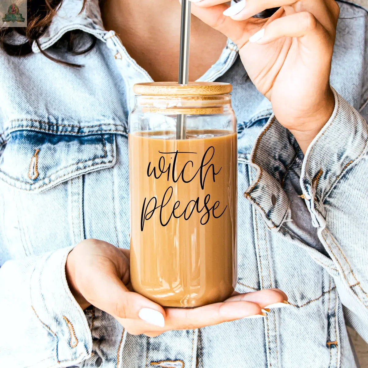 A person in a denim jacket holds an iced coffee in the "Witch Please 17oz" glass cup, featuring a bamboo lid and metal straw. The cursive "witch please" label adds magic to this stylish, eco-friendly setup.
