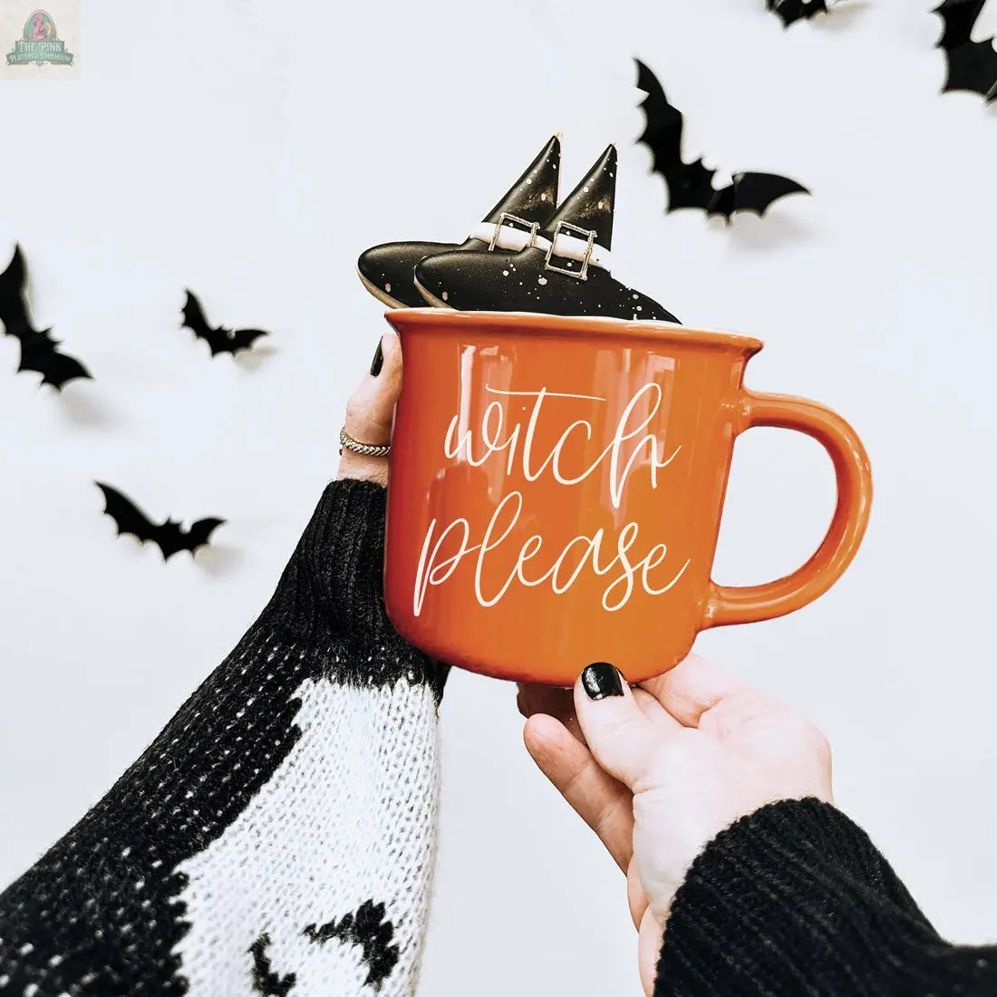 A person holding the Witch Please Mug, an orange ceramic mug topped with a tiny witch hat.