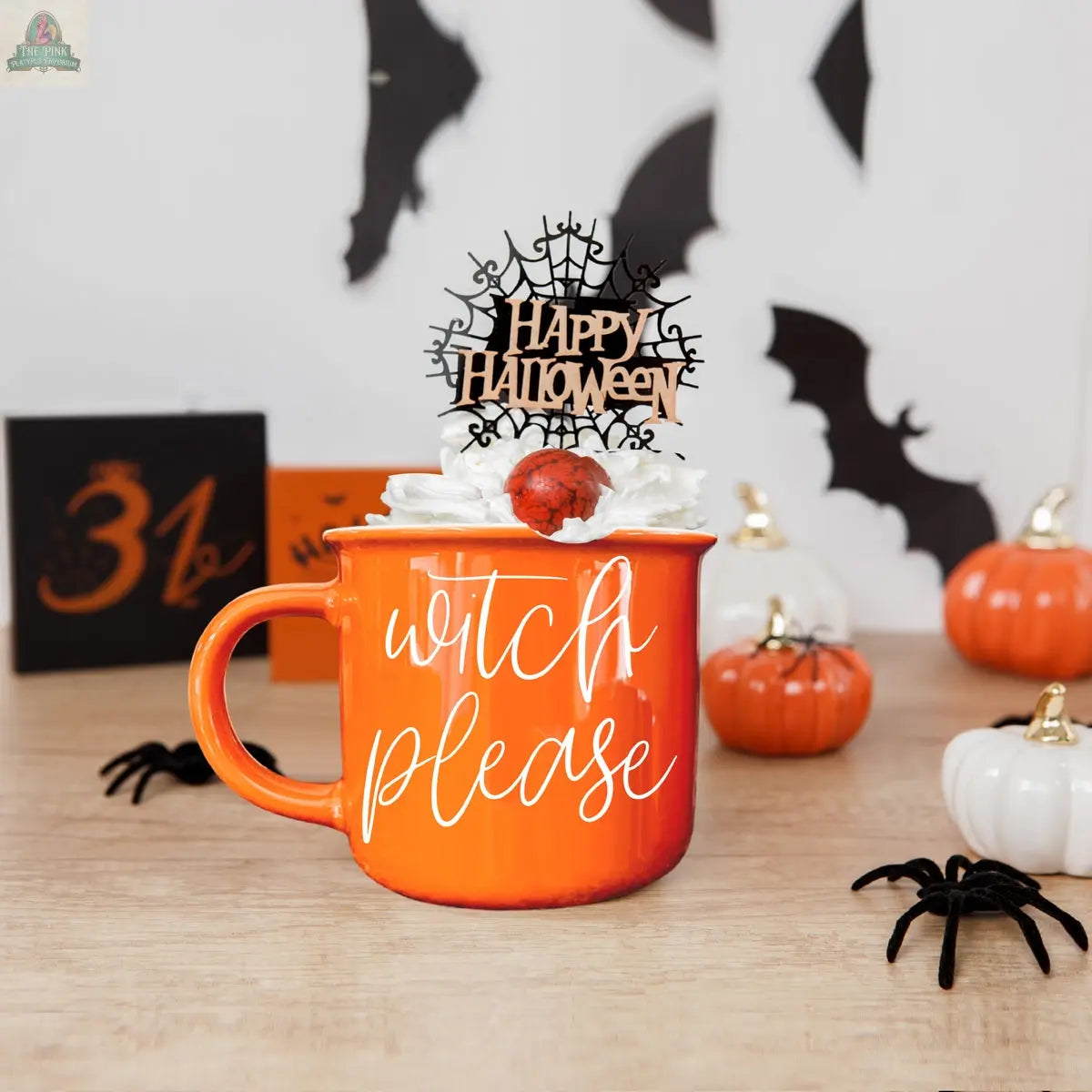 The Witch Please Mug is an orange ceramic mug featuring “witch please” text, topped with whipped cream, a strawberry, and a “Happy Halloween” topper. Halloween décor like pumpkins, bats, and a 31 sign appear in the background.