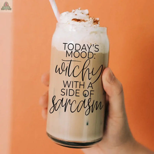 A hand holds the Witchy 20oz glass tumbler of iced coffee with whipped cream against a peach background. The tumbler reads "Today's mood: witchy with a side of sarcasm"—a perfect coffee gift for any witchy friend.