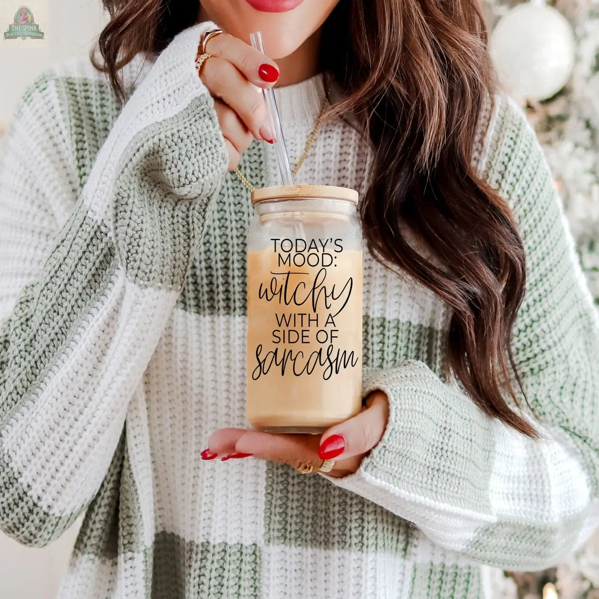 A woman in a striped sweater holds an eco-friendly Witchy 20oz tumbler of iced coffee with a straw. The jar reads, "Today's mood: witchy with a side of sarcasm." She has long hair and red nail polish—an ideal quirky witch gift.