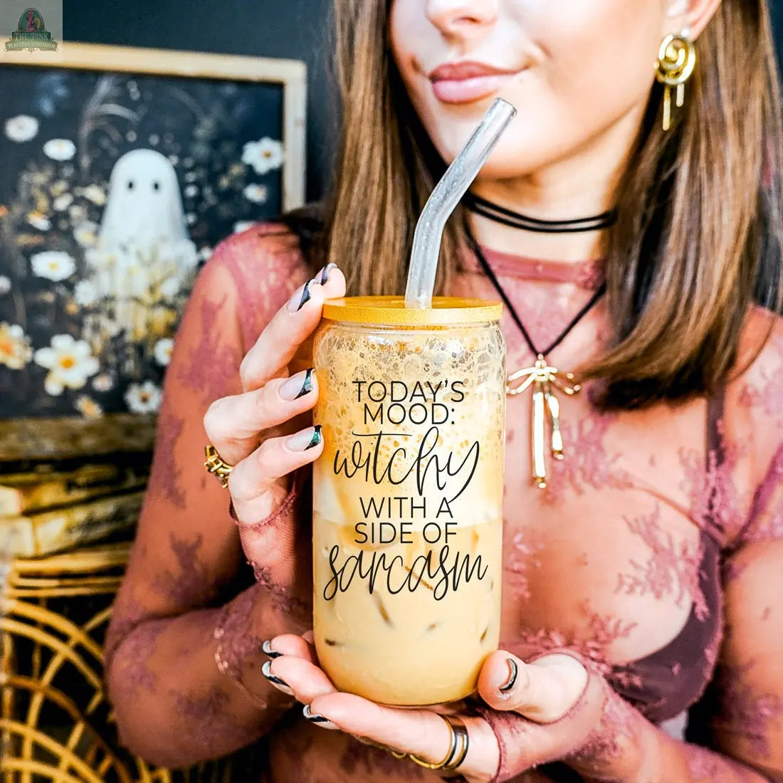 A woman in a sheer, floral-patterned top holds the Witchy 20oz tumbler, imprinted with "Todays mood: witchy with a side of sarcasm," alongside spooky ghost art—the perfect witch-themed gift.