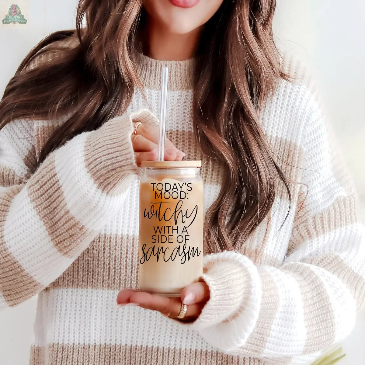 A woman in a beige and white striped sweater holds the Witchy 20oz eco-friendly tumbler reading "Today's mood: witchy with a side of sarcasm"—the perfect witch gift. Only her torso and lower face are visible.