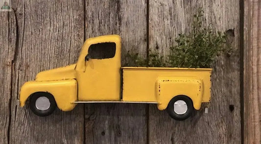 The Yellow Half Farm Truck wall decor features a rustic wooden background and green plants in its bed, bringing vintage charm to your home’s farmhouse-style decor.