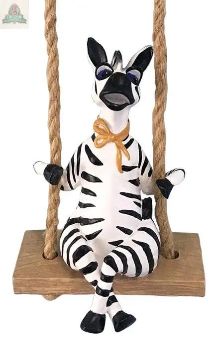 The Zebra Garden Swinger features a whimsical zebra with a yellow bow, sitting cross-legged on a wooden swing with rope handles—a cheerful handmade ceramic accent to brighten any space.