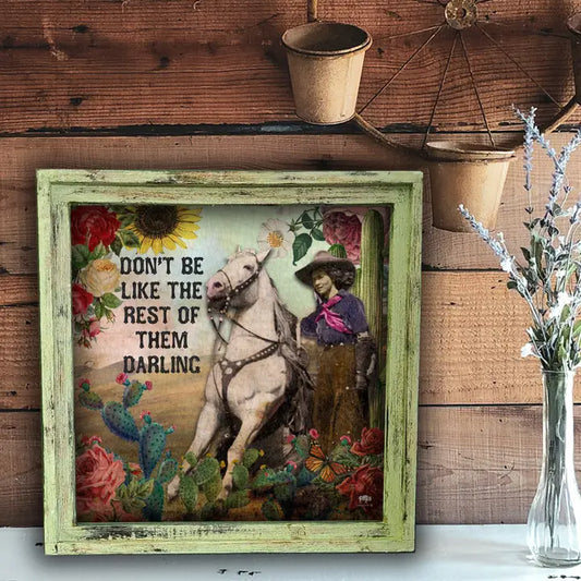 Decorative wall art with a woman on horseback and floral text against a wooden background.
