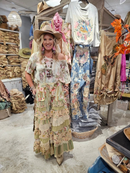 Woman in a boho western outfit standing in a store with clothing racks and decor.