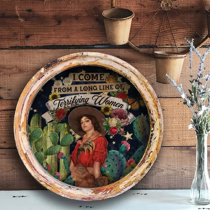 Western wall art with a woman in a cowboy hat and cacti, text 'I come from a long line of terrifying women', on a wooden background.