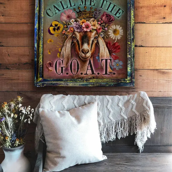 Decorative sign with a goat illustration and floral crown on a wooden wall above a sofa.