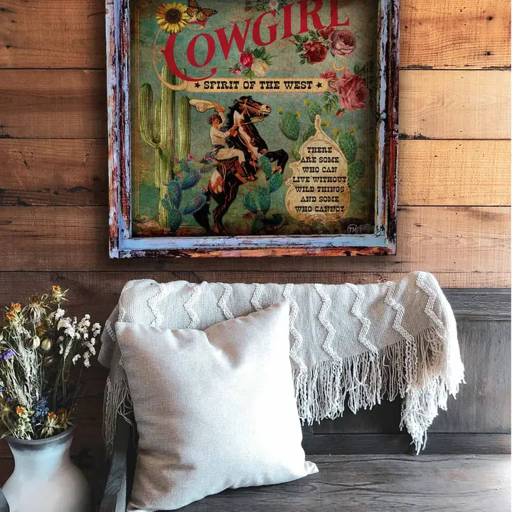Decorative wall art with a cowgirl theme above a couch with pillows and a blanket.