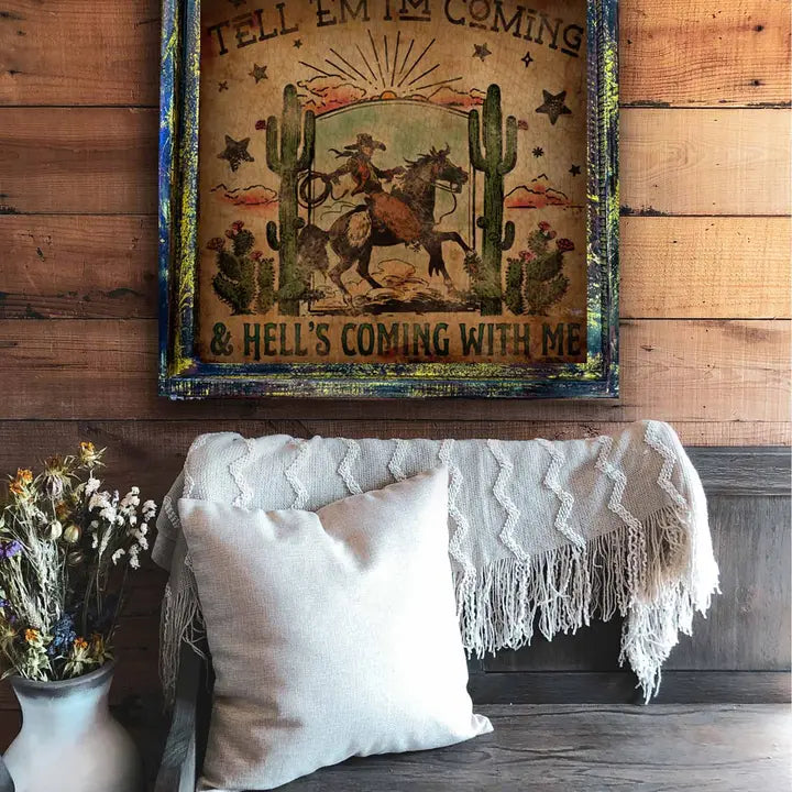 Decorative wall hanging with a cowboy and cactus design above a couch with pillows and a blanket.