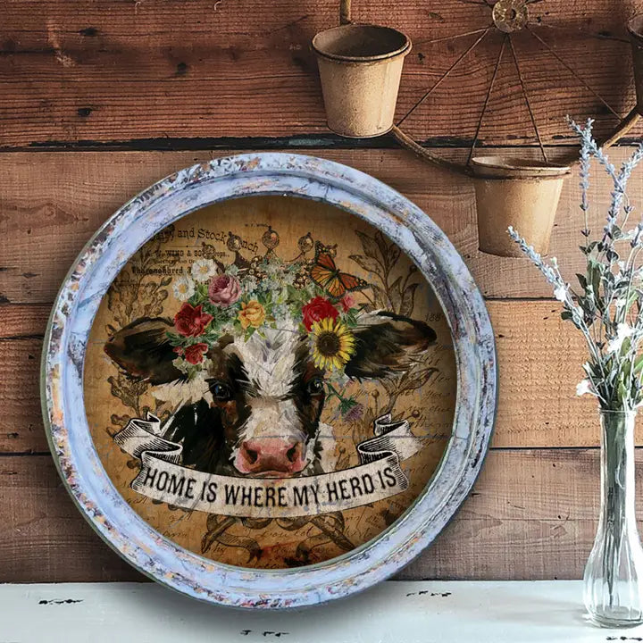 farmhouse wall decor with a cow illustration and 'Home is where my herd is' text on a wooden background.