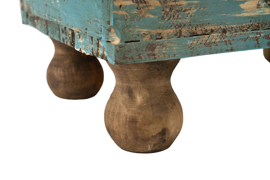 Close-up of a rustic wooden planter with peeling blue paint and large wooden legs.