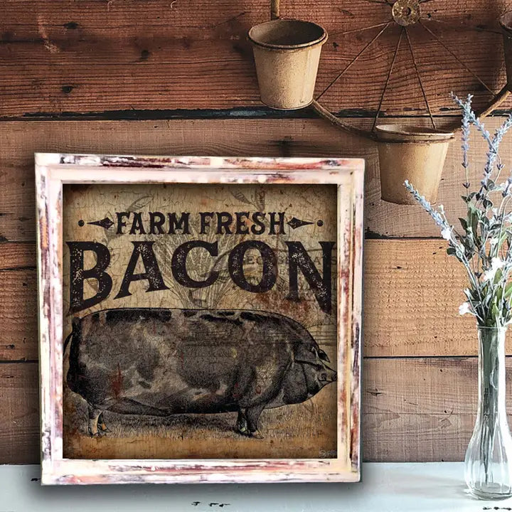 Framed sign with 'Farm Fresh Bacon' text and pig illustration on a wooden wall.