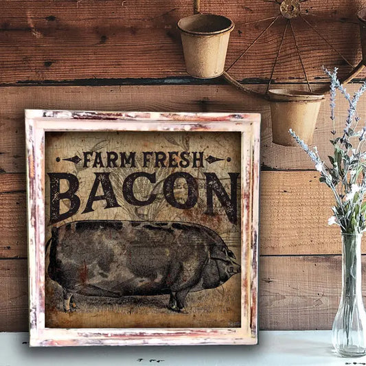 Framed sign with 'Farm Fresh Bacon' text and pig illustration on a wooden wall.