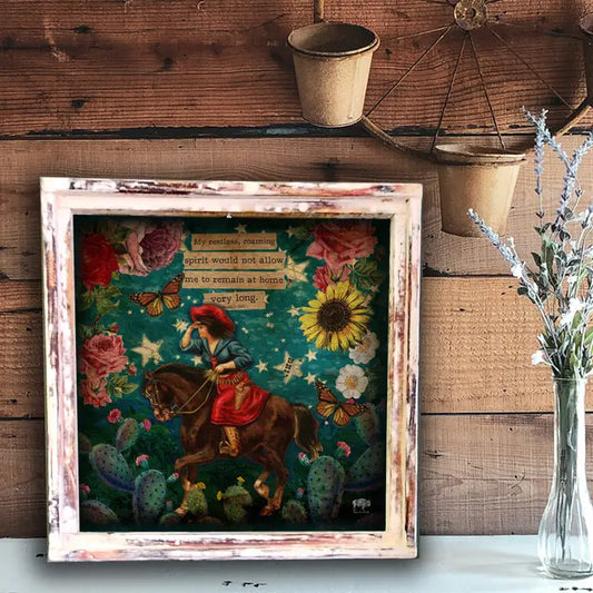 Framed artwork with a colorful scene of a person on horseback, flowers, and cacti against a wooden wall.
