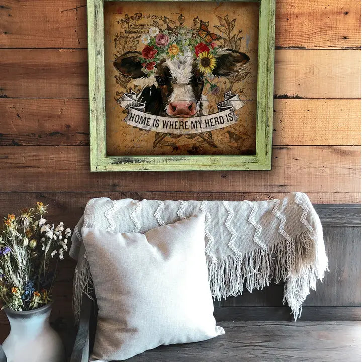 Framed artwork of a cow with flowers on a wooden wall above a sofa.