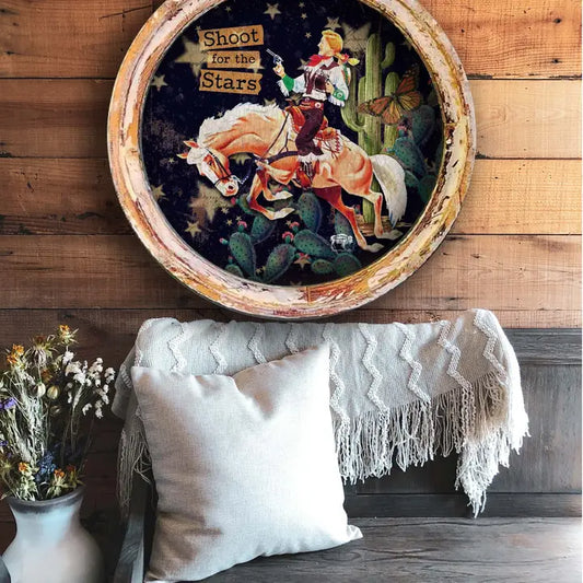 Decorative farmhouse wall decor piece with a cowgirl on horseback, cacti, and text 'Shoot for the Stars' on a wooden wall.