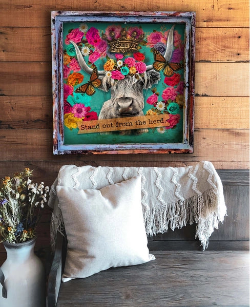 Decorative wall art with a cow's head surrounded by flowers on a wooden wall above a couch.